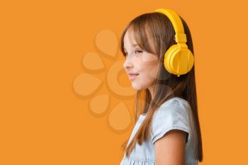 Little girl listening to music on color background�