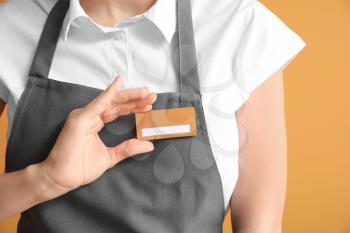 Young female waiter with blank badge on color background�