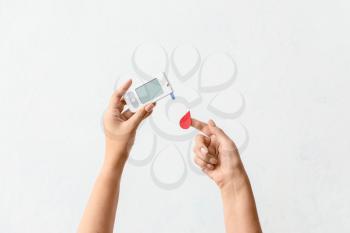 Female hands with glucometer and blood drop on light background. Diabetes concept�