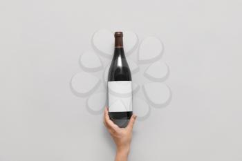Female hand and bottle of wine with blank label on light  background 