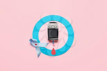 Glucometer with blue ring and awareness ribbon on color background. Diabetes concept�