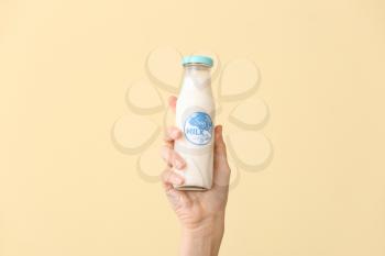 Female hand with bottle of soy milk on color background�