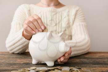 Woman putting coin into piggy bank on table, closeup�