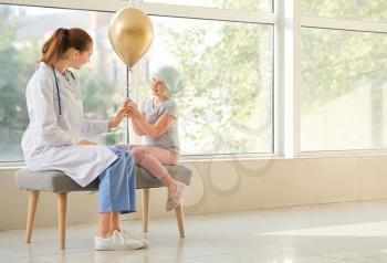 Doctor and little girl with golden balloon in clinic. Childhood cancer awareness concept�