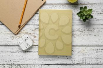 Blank book, earphones and plant on wooden background�