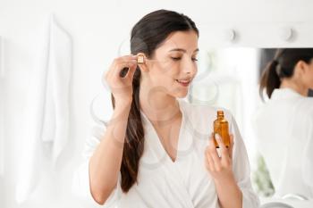 Beautiful young woman applying facial serum in bathroom�