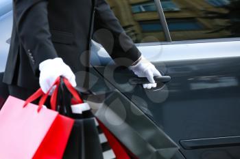 Chauffeur with shopping bags opening door of luxury car�