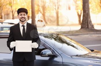 Handsome chauffeur with blank paper sheet near luxury car�
