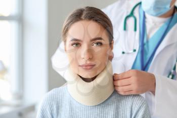 Doctor applying cervical collar on neck of young woman in clinic�