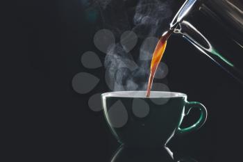 Pouring of hot coffee in cup on dark background�