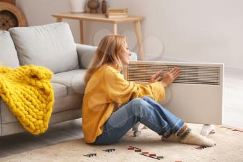 Mature woman near electric heater at home. Concept of heating season�