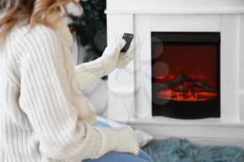 Young woman sitting near electric fireplace at home. Concept of heating season�
