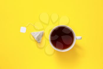 Cup of hot beverage and tea bag on color background�