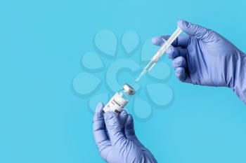 Doctor's hands with syringe and vaccine for immunization against COVID-19 on color background�