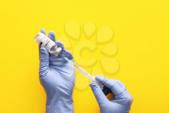 Doctor's hands with vaccine for immunization against COVID-19 on color background�