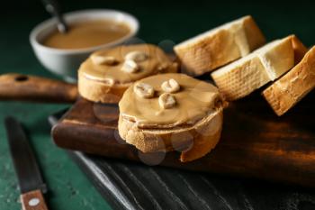 Boards with tasty bread and peanut butter on table, closeup�