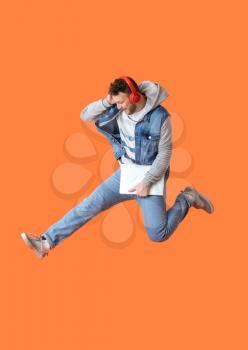 Jumping young man with laptop listening to music on color background�