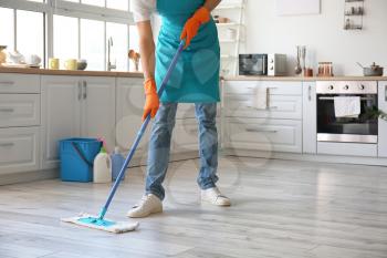 Young man mopping floor in kitchen�
