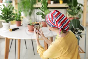 Young woman taking photo of her plants at home�
