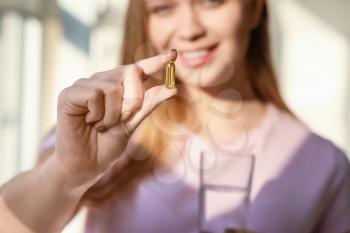 Young woman taking fish oil at home, closeup�