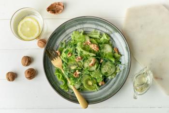 Plate with fresh salad and walnuts on light wooden background�