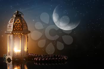 Muslim lamp and tasbih on table against night sky�