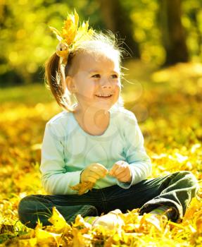 Cute little girl is playing with leaves in autumn park