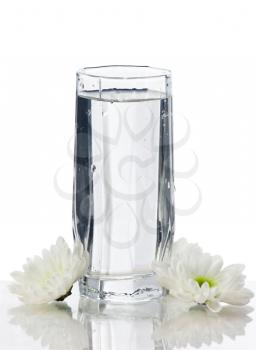 Glass of water with flowers on white