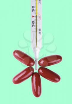 Close-up medical thermometer and tablets isolated on the green background