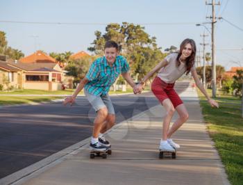 Happy brother and sister having fun with  skateboard on the street in the evening light