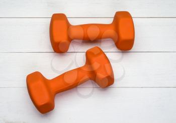 Two orange plastic coated dumbbells on white wooden background