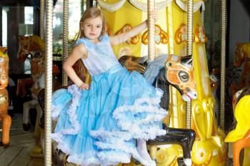 Pretty little girl in blue dress riding on a carousel
