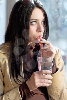 Portrait of beautiful young brunette drinking water through a straw. Isolated on white