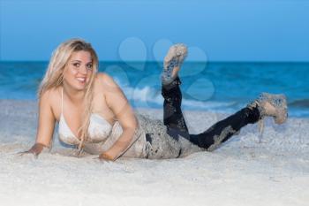 Smiling blond woman in wet clothes posing on the beach