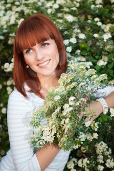 Attractive red-haired smiling woman posing near the flowering bush