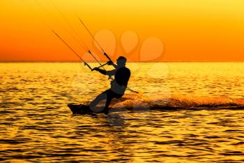 Silhouette of a kitesurfer sailing in the sea at sunset