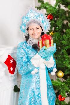 Smiling snow maiden posing near christmas fir with gift