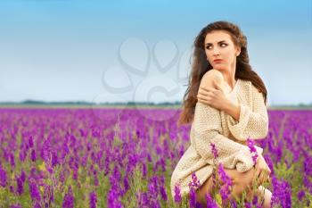 Attractive young brunette sitting in a flowering field and showing her shoulder