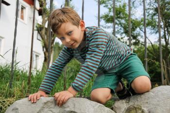 Little boy in striped sweater and shorts on big rocks