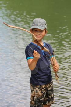 Smiling boy with arrows and bow near water of lake