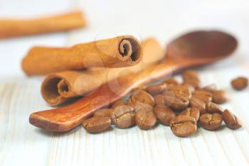 Coffee grains with wooden old-style spoon and cinnamon sticks on vintage table food ingredients background. Selective focus. Coffee aroma drink ingredients backdrop.