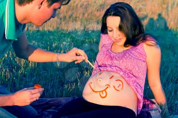 guy draws a face on a stomach of pregnant woman