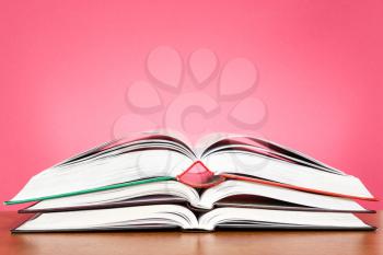 Open books on the wooden table over a  pink background