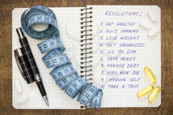 Resolutions written on a notepad with a measure tape and vitamin pills
