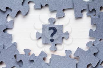 Jigsaw puzzle and question mark on wooden background