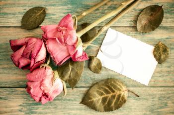 Old roses bouquet and blank greeting card over wooden table. Top view with copy space