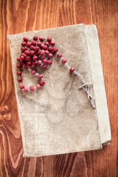 Old book and catholic rosary on wooden background