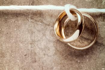 Wedding rings hanging on rope over a dirty canvas background