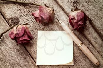 Old roses and blank sticky note with a pen. Top view with copy space.