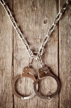 Handcuffs hanging on the chain against old wooden wall.